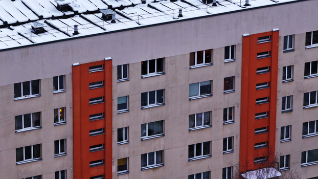 Aerial view of a multi story apartment building featuring orange vertical panels and a snow covered roof in Latvija. Aerial view of a multi story apartment building featuring orange vertical panels and a snow covered roof in Latvija.