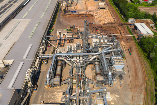 Aerial view of an industrial wood processing facility with complex piping systems storage yards for wood chips and large factory buildings in Jihlava Vysocina Region Czechia.