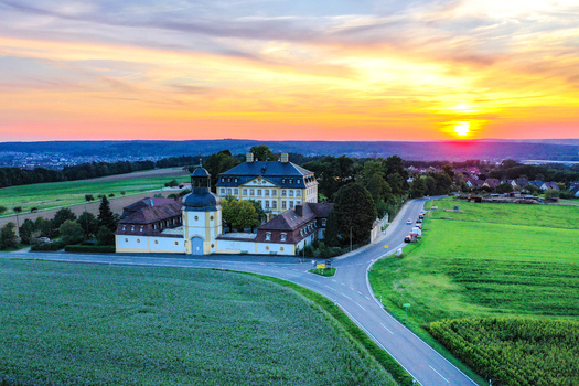 Aerial view of Schloss Jagersburg with its baroque architecture surrounded by green fields and trees during a vibrant sunset in Eggolsheim Bayern Germany.