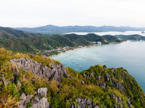 Aerial view of jagged limestone cliffs overlooking the turquoise waters of the bay with boats and the coastal town of El Nido Mimaropa Philippines.