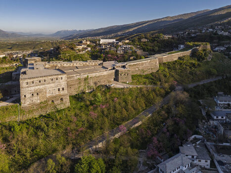 Aerial view of Gjirokaster Fortress a historic stone fortification perched on a hill surrounded by lush green slopes and the town of Gjirokaster Gjirokaster County Albania. Aerial view of Gjirokaster Fortress a historic stone fortification perched on a hill surrounded by lush green slopes and the town of Gjirokaster Gjirokaster County Albania.