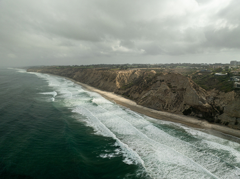 Aerial view of the rugged cliffs and breaking waves along the coastline under a cloudy sky at La Jolla Cove San Diego California United States. Aerial view of the rugged cliffs and breaking waves along the coastline under a cloudy sky at La Jolla Cove San Diego California United States.