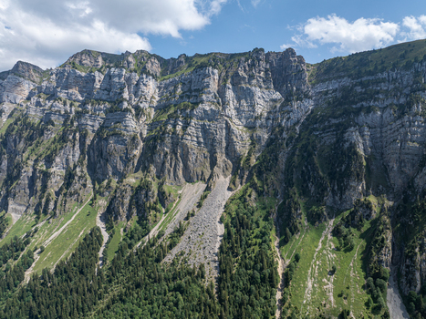 Aerial view of the dramatic limestone cliffs and steep scree slopes of the Justistal valley near the Niederhorn with lush alpine forests and meadows in Sigriswil Bern Switzerland. Aerial view of the dramatic limestone cliffs and steep scree slopes of the Justistal valley near the Niederhorn with lush alpine forests and meadows in Sigriswil Bern Switzerland.