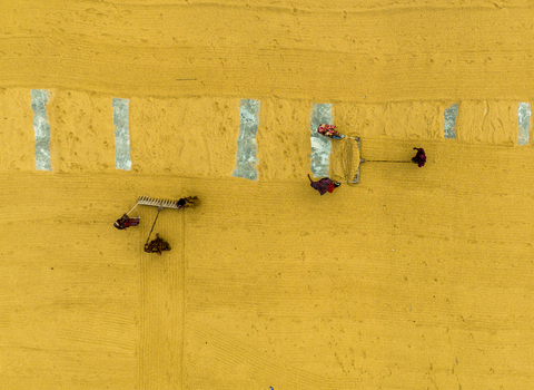 Ashuganj Chittagong Division Bangladesh 05 July 2022 Aerial view of workers raking and drying harvested rice on a large yellow surface.