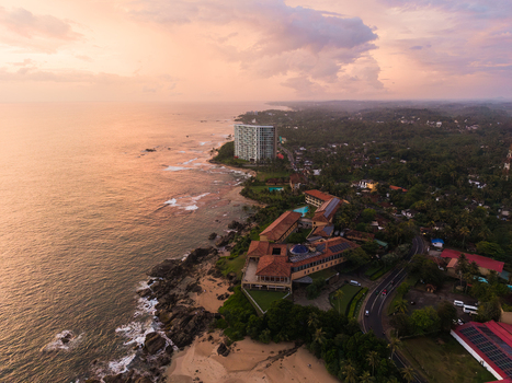 Aerial view of Gintota beach featuring a luxury resort complex rocky shoreline and lush tropical vegetation under a sunset sky Galle Southern Province Sri Lanka. Aerial view of Gintota beach featuring a luxury resort complex rocky shoreline and lush tropical vegetation under a sunset sky Galle Southern Province Sri Lanka.