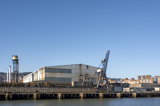 View of an industrial port facility with a large warehouse and a tall crane under a clear blue sky in Greater Bilbao Basque Country Spain. View of an industrial port facility with a large warehouse and a tall crane under a clear blue sky in Greater Bilbao Basque Country Spain.