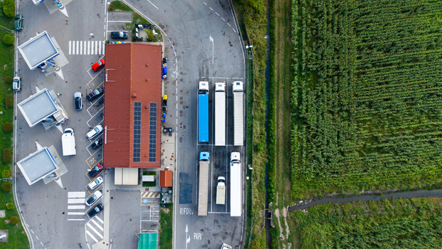 Aerial view of a truck parking area and fuel station with parked semi trucks cars and solar panels on the roof located next to a green field in Milan Lombardy Italy.