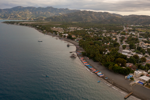 Aerial view of the coastline with colorful fishing boats docked on the beach palm trees and calm bay waters in Palmar de Ocoa Azua Province Dominican Republic.
