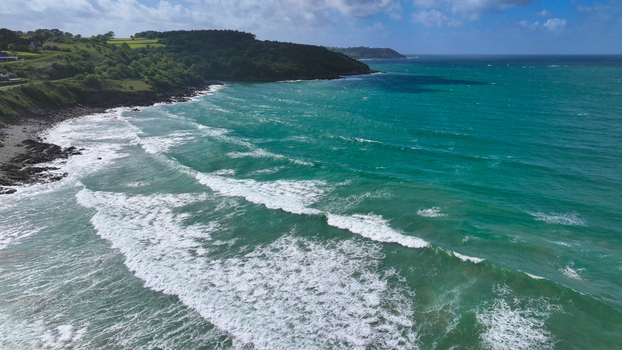 Aerial view of turquoise waves crashing on the rocky coastline with lush green hills in the background Locquirec Brittany France. Aerial view of turquoise waves crashing on the rocky coastline with lush green hills in the background Locquirec Brittany France.