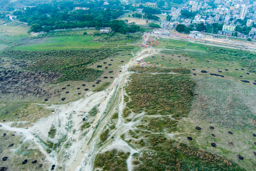 Aerial view of the open landscape with scattered vegetation and dirt paths leading towards the urban outskirts of Rajshahi Rajshahi Division Bangladesh.