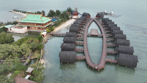 Aerial view of Pulau Lima Resort featuring overwater bungalows in an oval shape connected by wooden walkways surrounded by clear coastal waters in Kasemen Banten Indonesia. Aerial view of Pulau Lima Resort featuring overwater bungalows in an oval shape connected by wooden walkways surrounded by clear coastal waters in Kasemen Banten Indonesia.