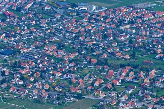 Aerial view of the dense tapestry of red tiled roofs contrasting with lush green spaces a sprawling suburban landscape under a soft diffused light Kintzheim Grand Est France.