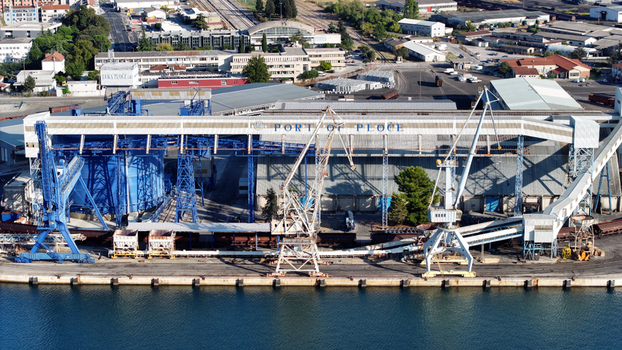 Aerial view of the Port of Ploce featuring industrial infrastructure large blue storage silos loading cranes and railway tracks along the waterfront in Croatia. Aerial view of the Port of Ploce featuring industrial infrastructure large blue storage silos loading cranes and railway tracks along the waterfront in Croatia.