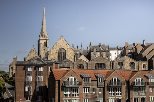 View of historic stone buildings and a church spire with modern brick residential apartments in the foreground under a clear blue sky Durham England United Kingdom. View of historic stone buildings and a church spire with modern brick residential apartments in the foreground under a clear blue sky Durham England United Kingdom.