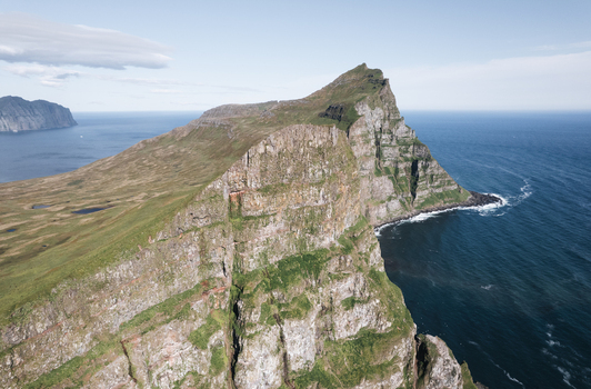 Aerial view of the dramatic Hornstrandir Nature Reserve featuring steep rocky cliffs and green grassy slopes overlooking the dark blue ocean in Isafjordur Isafjardarbaer Iceland. Aerial view of the dramatic Hornstrandir Nature Reserve featuring steep rocky cliffs and green grassy slopes overlooking the dark blue ocean in Isafjordur Isafjardarbaer Iceland.