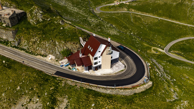 Aerial view of Transfagarasan mountain pass with a lodge on a sharp hairpin turn surrounded by green slopes and winding roads in Curtea de Arges Judetul Arges Romania. Aerial view of Transfagarasan mountain pass with a lodge on a sharp hairpin turn surrounded by green slopes and winding roads in Curtea de Arges Judetul Arges Romania.