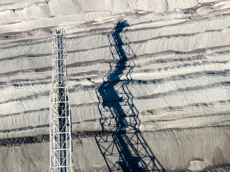 Aerial view of the Tagebau Welzow Sud brown coal open pit mine showing the conveyor belt structure and its long shadow cast across the layered earth strata in Spremberg Brandenburg Germany. Aerial view of the Tagebau Welzow Sud brown coal open pit mine showing the conveyor belt structure and its long shadow cast across the layered earth strata in Spremberg Brandenburg Germany.