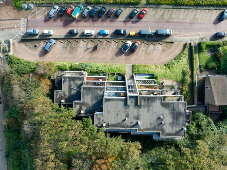 Aerial view of a modern residential building with flat roofs and balconies next to a parking lot and lush green trees in Wijk aan Zee North Holland Netherlands.