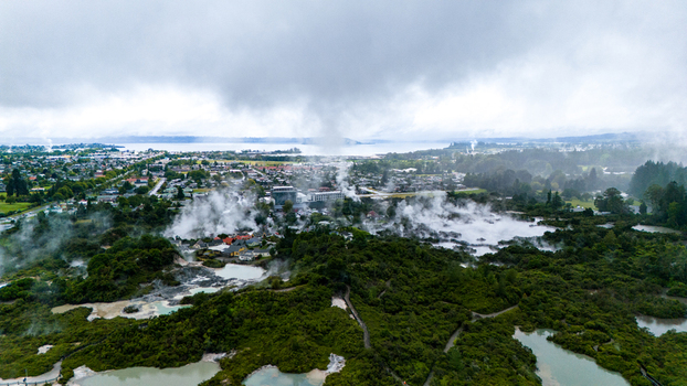 Aerial view of geothermal activity steaming through the landscape contrasting with the lush greenery and the distant lake under a cloudy sky Rotorua New Zealand. Aerial view of geothermal activity steaming through the landscape contrasting with the lush greenery and the distant lake under a cloudy sky Rotorua New Zealand.