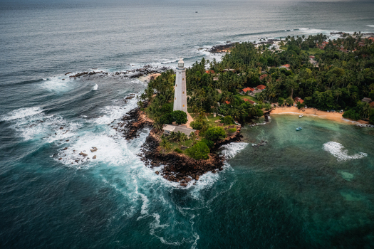 Aerial view of Dondra Lighthouse standing on a rocky headland surrounded by lush palm trees crashing waves and turquoise waters in Dondra Southern Province Sri Lanka. Aerial view of Dondra Lighthouse standing on a rocky headland surrounded by lush palm trees crashing waves and turquoise waters in Dondra Southern Province Sri Lanka.