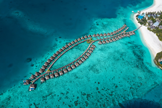 Aerial view of overwater bungalows arranged in a curved pattern over the turquoise lagoon of a tropical resort in Kudahuvadhoo Dhaalu Atoll Maldives. Aerial view of overwater bungalows arranged in a curved pattern over the turquoise lagoon of a tropical resort in Kudahuvadhoo Dhaalu Atoll Maldives.
