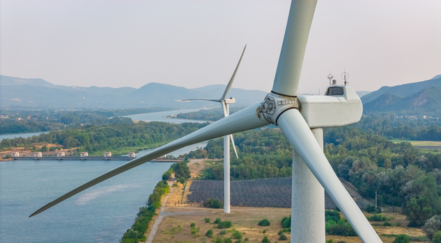 Aerial view of a wind turbine in the foreground with solar panels the Rhone River dam a second wind turbine and a mountain landscape in Le Pouzin Auvergne Rhone Alpes France.