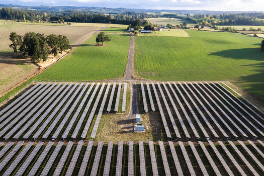 Aerial view of a large solar farm with rows of photovoltaic panels situated in a rural landscape with green fields trees and a dirt road in Woodburn Oregon United States. Aerial view of a large solar farm with rows of photovoltaic panels situated in a rural landscape with green fields trees and a dirt road in Woodburn Oregon United States.