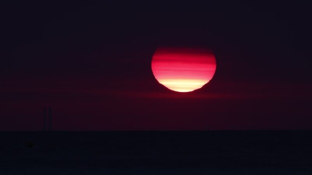 View of a vibrant red sun over the dark horizon France.