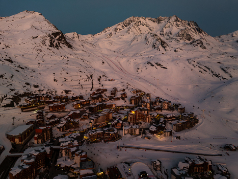 Aerial view of a village nestled amongst snow covered mountains the orange glow of the buildings contrasting the cool blue twilight sky Val Thorens Auvergne Rh&ocirc;ne Alpes France.