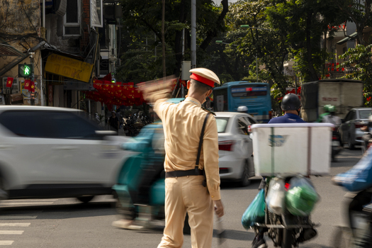 View of a traffic police officer in uniform directing the flow of vehicles and scooters on a busy street in Hanoi Ha Noi Vietnam.