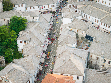 Aerial view of the narrow cobblestone streets and traditional stone tiled rooftops of the old bazaar with people at outdoor cafes in Gjirokaster Gjirokaster County Albania. Aerial view of the narrow cobblestone streets and traditional stone tiled rooftops of the old bazaar with people at outdoor cafes in Gjirokaster Gjirokaster County Albania.