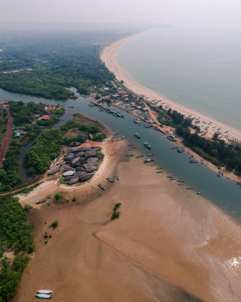 Aerial view of the river mouth meeting the Arabian Sea with fishing boats anchored along the banks surrounded by mangroves and a sandy coastline in Vengurla Maharashtra India. Aerial view of the river mouth meeting the Arabian Sea with fishing boats anchored along the banks surrounded by mangroves and a sandy coastline in Vengurla Maharashtra India.