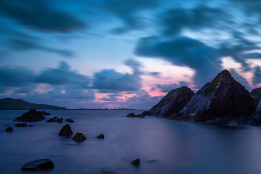 View of the rugged coastline and rocky cliffs at twilight under a dramatic cloudy sky in Dun Chaoin County Kerry Ireland. View of the rugged coastline and rocky cliffs at twilight under a dramatic cloudy sky in Dun Chaoin County Kerry Ireland.