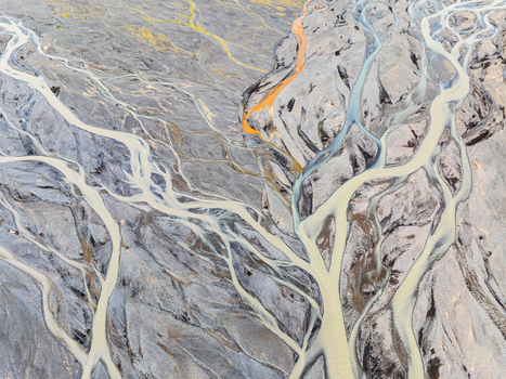 Aerial view of a glacial braided river with intricate water channels and sediment patterns flowing through a volcanic landscape in Iceland. Aerial view of a glacial braided river with intricate water channels and sediment patterns flowing through a volcanic landscape in Iceland.