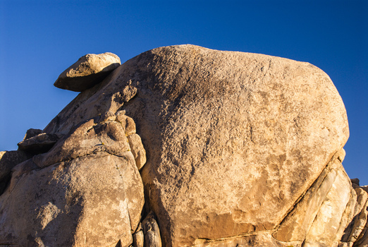 View of a large textured rock formation under a clear blue sky during golden hour in Joshua Tree California United States.