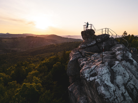 Aerial view of a person standing on the Popova Skala rock formation at sunset overlooking the surrounding forest and rolling hills in Hradek nad Nisou Liberec Region Czechia. Aerial view of a person standing on the Popova Skala rock formation at sunset overlooking the surrounding forest and rolling hills in Hradek nad Nisou Liberec Region Czechia.
