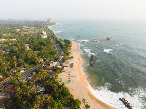 Aerial view of the tropical coastline with a sandy beach coastal road and lush palm trees in Galle Southern Province Sri Lanka.
