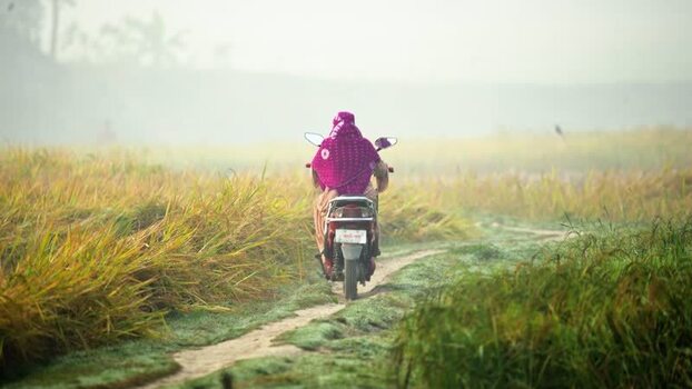 View of a woman riding a motorcycle through rural fields Bangladesh. View of a woman riding a motorcycle through rural fields Bangladesh.