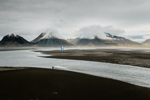 Aerial view of Vestrahorn with a kitesurfer gliding across the shallow water and dark sandbars under a dramatic cloudy sky in Sveitarfelagid Hornafjordur Iceland. Aerial view of Vestrahorn with a kitesurfer gliding across the shallow water and dark sandbars under a dramatic cloudy sky in Sveitarfelagid Hornafjordur Iceland.