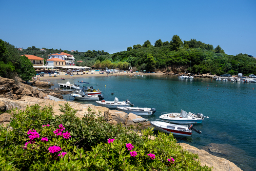 View of Pelion bay with small motorboats moored near a sandy beach and lush green hills in Magnesia Prefecture Greece. View of Pelion bay with small motorboats moored near a sandy beach and lush green hills in Magnesia Prefecture Greece.