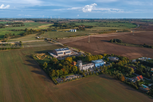 Aerial view of a rural industrial complex with a tower solar panels and parking area surrounded by agricultural fields and distant wind turbines in Uckermark Brandenburg Germany. Aerial view of a rural industrial complex with a tower solar panels and parking area surrounded by agricultural fields and distant wind turbines in Uckermark Brandenburg Germany.