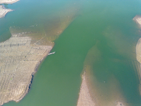 Aerial view of the Karanganyar reservoir with green water exposed mudflats and a small boat moored near the shore in Wadaslintang Central Java Indonesia. Aerial view of the Karanganyar reservoir with green water exposed mudflats and a small boat moored near the shore in Wadaslintang Central Java Indonesia.