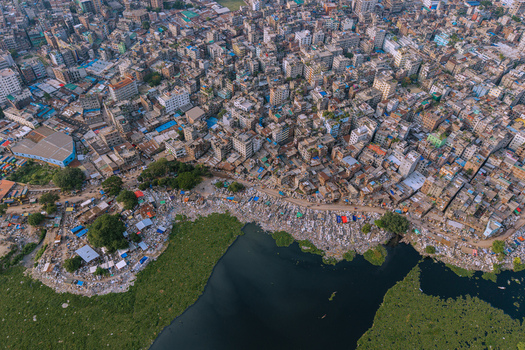 Aerial view of the Buriganga River flowing past dense urban housing and colorful rooftops in Keraniganj Dhaka Division Bangladesh. Aerial view of the Buriganga River flowing past dense urban housing and colorful rooftops in Keraniganj Dhaka Division Bangladesh.