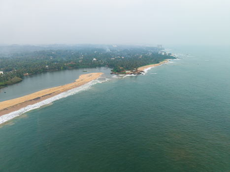 Aerial view of the sandy coastline where a river meets the turquoise ocean waves and lush tropical palm trees Galle Southern Province Sri Lanka.