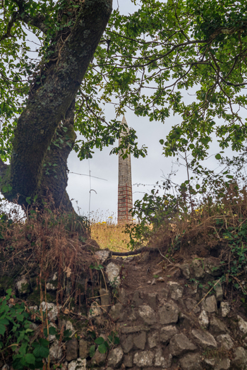 View of the Bodmin Beacon obelisk monument framed by tree branches and a stone wall in Bodmin Cornwall United Kingdom. View of the Bodmin Beacon obelisk monument framed by tree branches and a stone wall in Bodmin Cornwall United Kingdom.