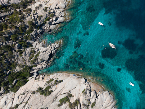 Aerial view of the rugged rocky coastline and crystal clear turquoise waters of San Teodoro with small boats anchored near the shore in San Teodoro Sardegna Italy.
