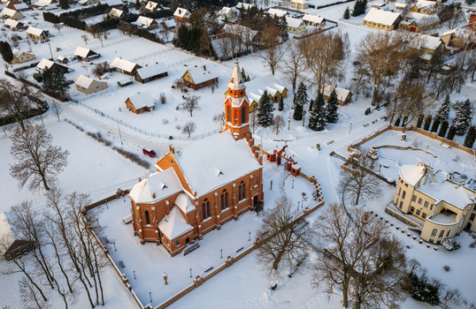 Aerial view of the red brick Church of the Virgin Mary of the Scapular surrounded by snow covered houses and bare trees in a winter landscape Kernave Vilnius County Lithuania.