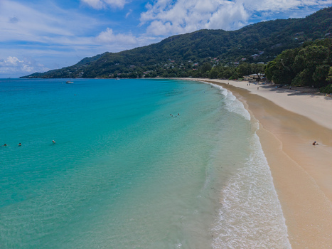 Aerial view of the turquoise sea meeting the sandy shore under the gaze of lush green mountains Beau Vallon Beach Victoria Seychelles. Aerial view of the turquoise sea meeting the sandy shore under the gaze of lush green mountains Beau Vallon Beach Victoria Seychelles.