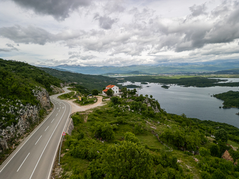Aerial view of Slansko Lake with a winding road a white house with a red roof and surrounding green hills under a cloudy sky in Niksic Municipality Montenegro. Aerial view of Slansko Lake with a winding road a white house with a red roof and surrounding green hills under a cloudy sky in Niksic Municipality Montenegro.