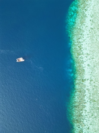 Aerial view of a small boat floating in the deep blue sea next to the vibrant coral reef of Pulau Ndaa in Tomia South East Sulawesi Indonesia.